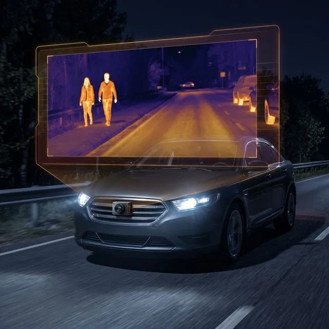 Car at night with a thermal camera view showing pedestrians on the road